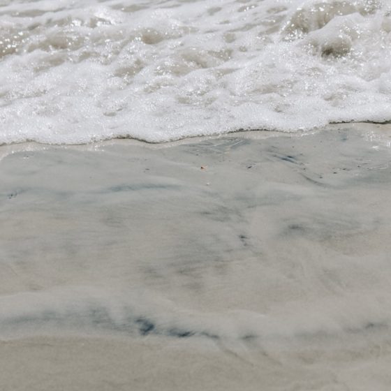 Close up of beach shore with sand and wave rolling in.