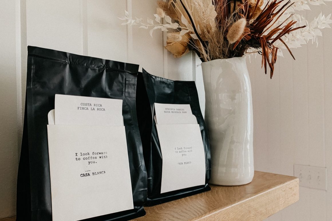 Two bags of coffee and a ceramic vase with dried flowers sit on a wooden shelf.
