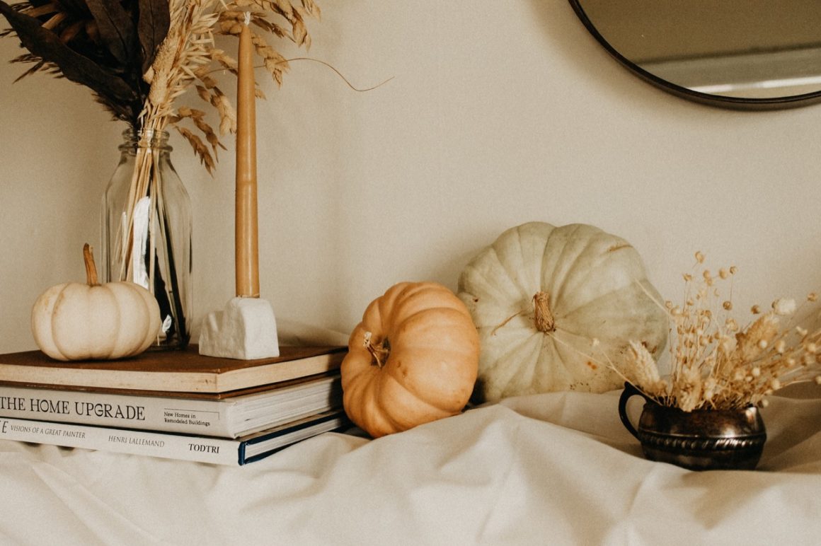 Fireplace mantel decorated with fabric, lights, books, pumpkins, and dried grasses.