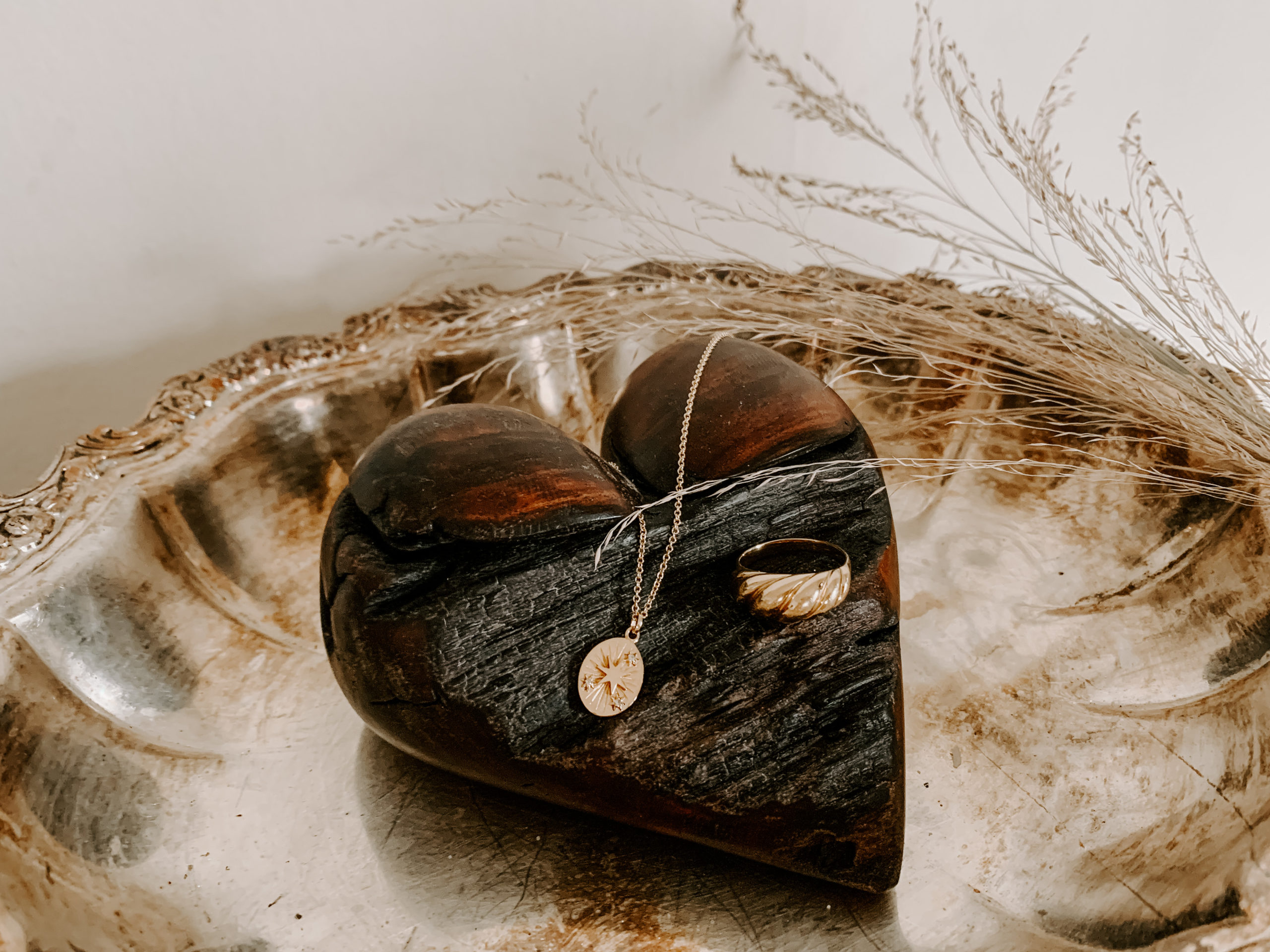 wooden heart lays on silver tray with gold jewelry draped over it